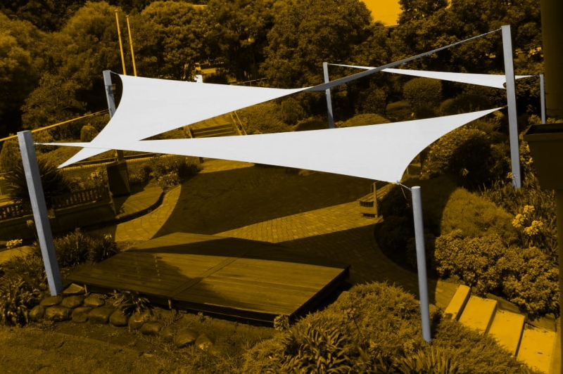 White triangular sun shade sail 5x5x7 m stretched over a garden terrace, providing shade and UV protection.