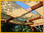 Beige HDPE zonneschermdoek 0,5x5 m gemonteerd op een houten pergola in de tuin.