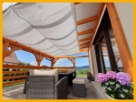 Αδιάβροχο επεκτεινόμενο πανί σκίασης κήπου 3x3 m τοποθετημένο κάτω από στέγαστρο βεράντας με έπιπλα rattan και λουλούδια.