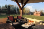 Închidere de terasă transparentă la comandă pentru pavilion cu fotolii, măsuță de cafea și vedere la grădină.