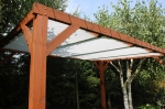 Maatwerk wit voordelig schaduwdoek gemonteerd op een bruine houten pergola in de tuin.
