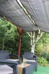 Grått uttrekkbart HDPE solseil montert på en trepergola over en gruppe kunstrottingmøbler.