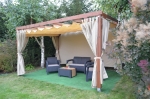 Beige waterdicht gordijn op maat gemonteerd op een houten tuinpergola met loungetuinmeubels.