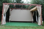 Водоустойчива завеса по поръчка, монтирана върху дървена градинска пергола, с дървета и зелена трева на заден план.