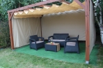 Bahçe mobilyalarının üzerine, pergola altına monte edilmiş özel yapım bej yatay HDPE Roma jaluzi. Zeminde yapay çim.