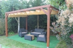 Braune Holzpergola im Garten mit beigefarbenem HDPE-Horizontal-Faltrollo nach Maß über Gartenmöbeln.