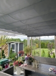 Graue Beschattung nach Maß für Wintergärten, montiert unter einer Terrassenüberdachung mit Blick in den Garten.
