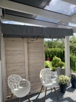 Custom-made grey shading cover mounted under the glass roof of a winter garden over a terrace with furniture.