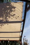 Μπεζ πανί σκίασης HDPE κατά παραγγελία τοποθετημένο σε ξύλινη πέργκολα παρέχει σκιά μια ηλιόλουστη μέρα.