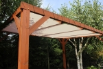 Toldo vela de HDPE marrón claro a medida instalado en una estructura de pérgola de madera en un jardín.