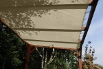 Beige HDPE solsejl på mål monteret på en træpergola i haven.