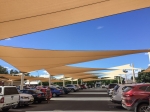 Voiles d'ombrage beiges sur mesure pour carports protégeant les voitures sur le parking par une journée ensoleillée.