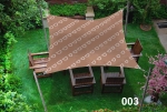 Vela ombreggiante quadrata marrone 3x3 con motivo bianco, montata sopra mobili in legno sul prato.