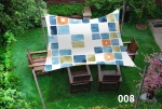 Waterproof 3x3 m sun sail with colourful squares, mounted over wooden garden furniture.