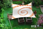 Vela ombreggiante quadrata 3x3m con grafica a spirale sopra mobili da giardino in legno su un prato verde.