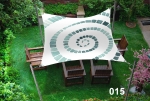 Square sun sail 3x3 m with green spiral graphic over wooden garden furniture.