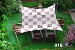 Voile d'ombrage carrée 3x3 m imperméable avec motif à pois marrons au-dessus de meubles en bois sur une pelouse.