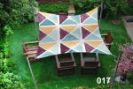 Square waterproof 3x3 m sail shade with geometric patterns over wooden garden furniture on a green lawn.