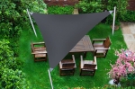 Vela de sombra triangular gris impermeable que protege los muebles de madera en una terraza rodeada de vegetación.