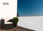 Balkonscherm met wit geometrisch patroon gemonteerd op een terrasleuning naast een moderne fauteuil en een plant.