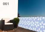 Brise-vue de balcon bleu clair avec motif quadrillé blanc, monté sur une rambarde en métal avec un fauteuil et une plante.