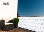 Wit raster balkonscherm met sterretjespatroon, gemonteerd op een balkon met fauteuil en plant. Product op maat.