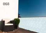 Raster balkonafscherming op maat in lichtblauw met witte kruisjes op een modern balkon naast een fauteuil.