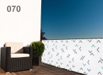 Balcony privacy screen with geometric pattern, armchair and green bush against a blue sky.