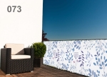 Wit-blauw balkonscherm met bladmotief op een terras met vlechtwerk fauteuil en struik in pot.