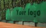 Yoğun bitki örtüsü önünde örnek logolu, yeşil renkte özel yapım tenis kortu rüzgarlığı.