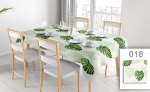 Toalha de mesa publicitária por medida com motivo de folhas de monstera, numa mesa numa sala de jantar luminosa com cadeiras brancas e loiça.