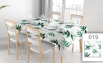 Mantel publicitario con estampado de hojas verdes sobre fondo blanco, mesa puesta con sillas en un interior moderno y luminoso.