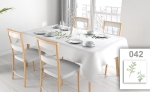 Mantel publicitario blanco con estampado vegetal sobre mesa de comedor con vajilla y cuatro sillas.