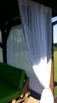 White, openwork made-to-measure net curtain hanging in a garden gazebo next to a green pallet sofa.