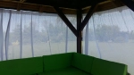 Custom-made white voile curtain hanging in a wooden garden gazebo with a green corner sofa.