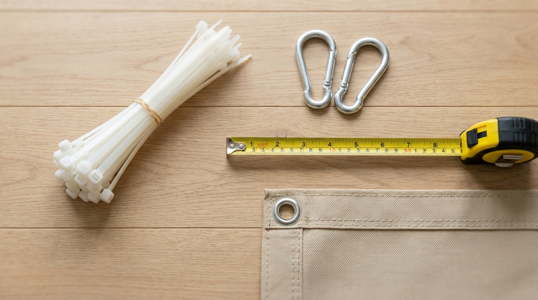 Cable ties, carabiner clips, measuring tape and a fabric privacy screen arranged on a wooden surface.
