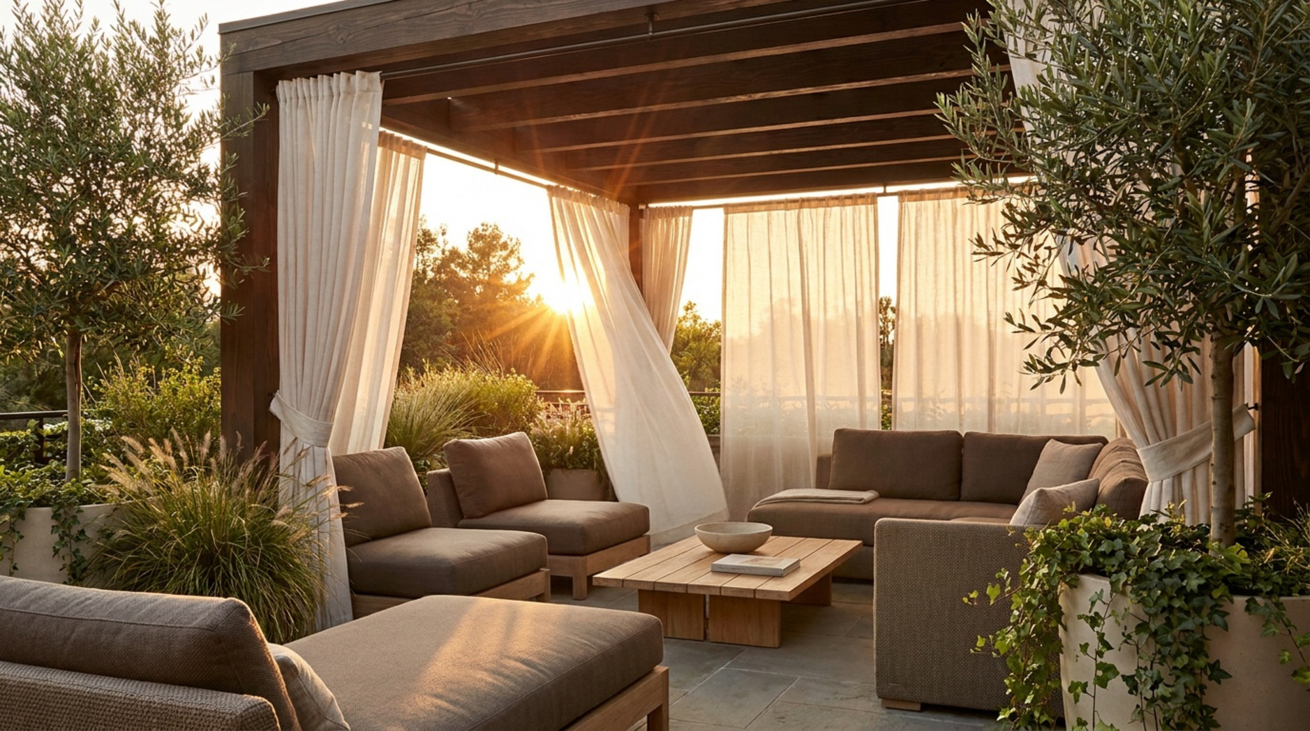 Wooden garden pergola with white curtains, neutral outdoor sofas and a coffee table at sunset