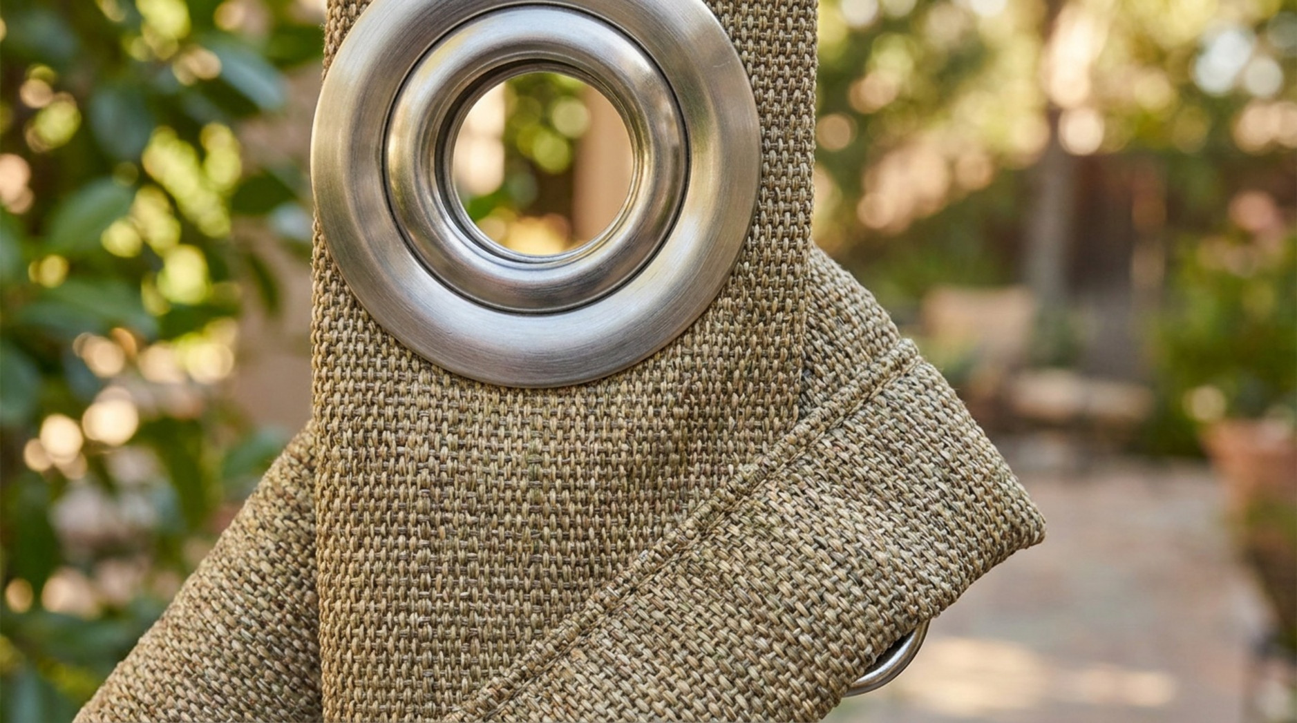 Close-up of a large silver eyelet fitted into textured beige outdoor curtain fabric