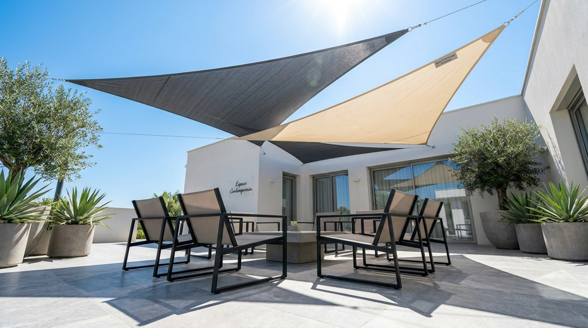 Voiles d’ombrage triangulaires grises et beiges installées au-dessus d’une terrasse moderne avec mobilier extérieur