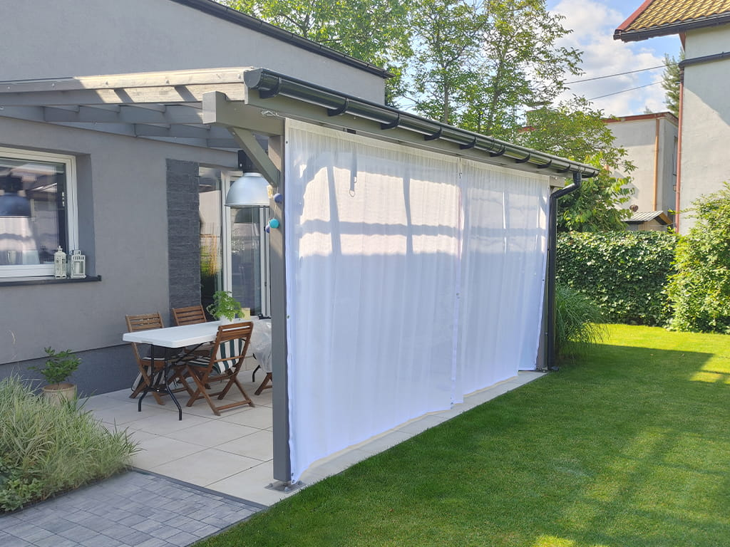 Auvent de terrasse avec des rideaux blancs translucides, offrant une protection légère et de l'intimité sur un patio pavé.