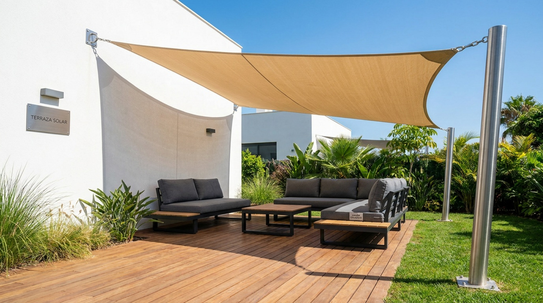 Toldo vela beige instalado sobre una terraza de madera con sofás exteriores y jardín.