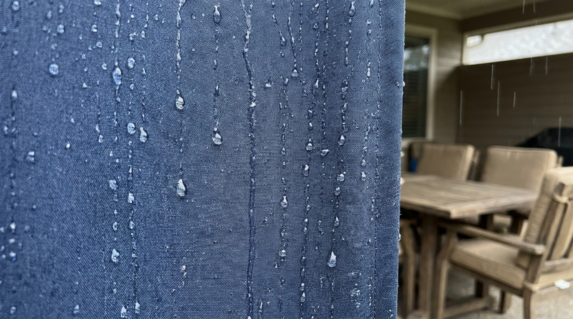 Close-up of raindrops running down blue water-repellent outdoor curtain fabric